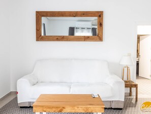 Ein weißes Sofa, ein Holztisch und ein spiegel mit Holzrahmen in einem Raum mit einem gemusterten Boden.