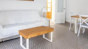 Ein weißes Sofa, ein Holztisch, ein weißer Esstisch mit Stühlen und ein gemusterter Boden.