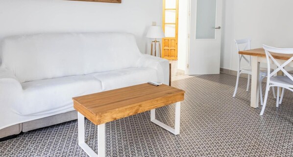 Ein weißes Sofa, ein Holztisch, ein weißer Esstisch mit Stühlen und ein gemusterter Boden.