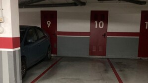 Een parkeergarage met genummerde deuren, een blauwe auto geparkeerd voor deur nummer 9, en een betonnen vloer met rode lijnen.