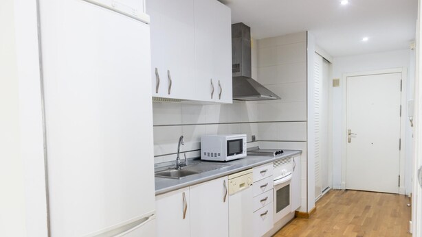 Een keuken met witte kastjes, een magnetron, een fornuis en een spoelbak.