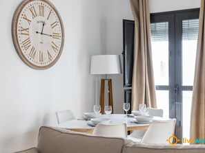 Zona pranzo con tavolo rotondo apparecchiato per quattro persone, una sveglia a parete e una lampada.