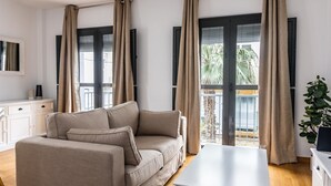 Een moderne woonkamer met een beige bank, een witte salontafel en een balkon met gordijnen.