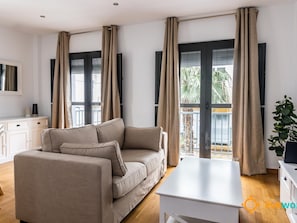 Ein modernes Wohnzimmer mit einem beigefarbenen Sofa, einem weißen Couchtisch und einem Balkon mit Vorhängen.