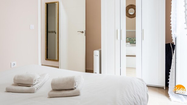 A bedroom with a bed, two towels, a wardrobe, and a mirror. - Corralon de Los Carros by Cadiz Time A (Cádiz)