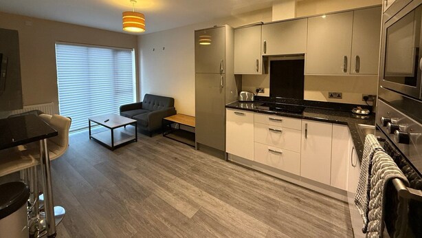 Eine moderne Küche mit weißen Schränken, einer schwarzen Arbeitsplatte und einem eingebauten Backofen. Es gibt einen Essbereich mit Tisch und Stühlen sowie eine Couch.