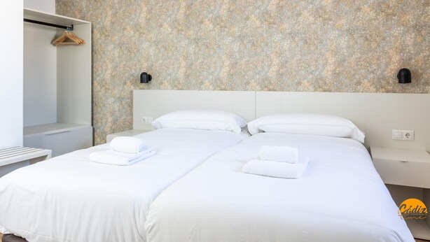 A hotel room with a large bed, two bedside tables, a wardrobe, and a floral-patterned wall. - Mar de La Vi a Free Parking by C diz Time (Cádiz)
