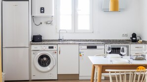 A modern kitchen with a washing machine, dishwasher, and a dining area with a table set for two. - Mar de La Vi a Free Parking by C diz Time (Cádiz)