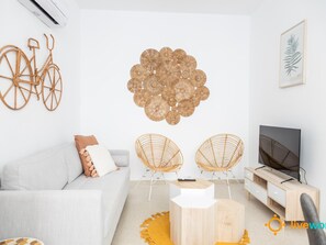 A modern living room with a white sofa, two wicker chairs, a coffee table, and a TV stand. - Apartamento Bike by Livework (Cádiz)