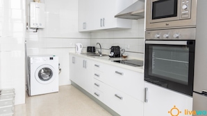 A modern kitchen with white cabinets, a built-in washing machine, a microwave, and an oven. - Apartamento Bike by Livework (Cádiz)