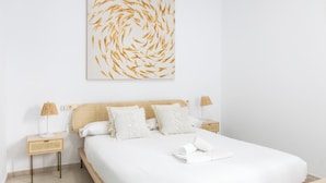 A neatly arranged hotel room with a large bed, two bedside tables with lamps, and a wall-mounted artwork. - Apartamento Bike by Livework (Cádiz)