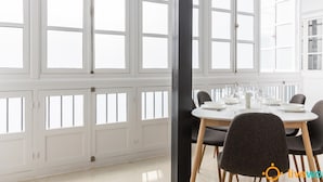 A dining area with a round table set for six, surrounded by chairs. Large windows with multiple panes allow natural light to fill the room. - Apartamento Bike by Livework (Cádiz)