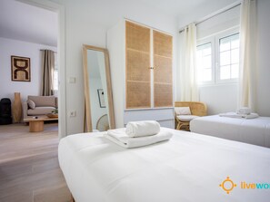 Ein Hotelzimmer mit zwei Betten, einem großen Spiegel, einer Rattan-Trennwand, einem Sofa und einem Sessel.