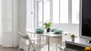 A bright, white room with a dining table set for two, a potted plant, and a TV on a stand. - Flamenco Centro by Cadiz Time (Cádiz)