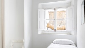 A small, white room with a single bed, a window with open shutters, and a white chair. - Flamenco Centro by Cadiz Time (Cádiz)