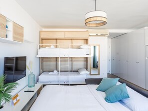 Una habitación de hotel moderna con una cama litera, una cama de matrimonio, un televisor, un escritorio y un armario.