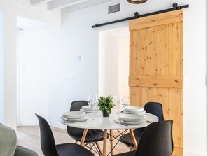 Ein Essbereich mit einem runden Tisch, gedeckt für vier Personen, schwarzen Stühlen und einer Holztür im Hintergrund.