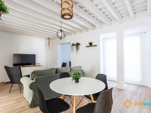Ein modernes Wohnzimmer mit einer Couch, Sesseln, einem Fernseher und einem Esstisch mit Stühlen.
