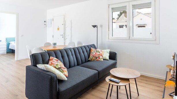 Een moderne woonkamer met een donkergrijze bank, een ronde houten salontafel, en een eethoek met een witte tafel en stoelen.