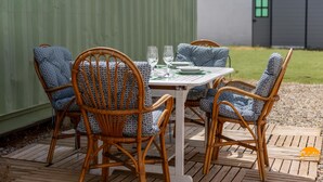 Een terras met een tafel en vier rieten stoelen, elk met een gestreept kussen.