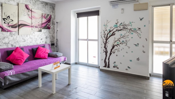 A modern living room with a purple sofa, a white coffee table, and a wall with floral and tree decals. - Modern Haven Loft by Cadiz Time (Cádiz)