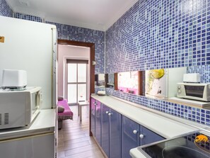 Eine Küche mit blauen Fliesen an der Spritzschutzwand, weißen Geräten und Blick auf einen Balkon.