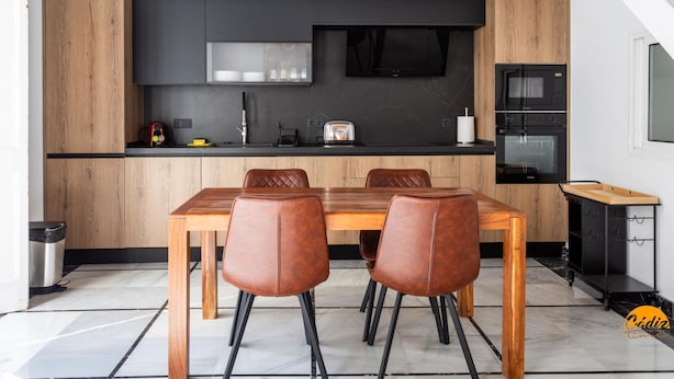 Een moderne keuken met een eethoek, met een houten tafel en stoelen, een zwart aanrecht en een ingebouwde oven.