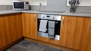 Cucina con mobili in legno, forno a microonde, forno e zoccolo in piastrelle.