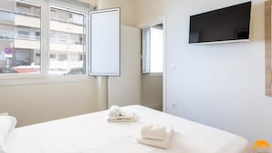 A hotel room with a bed, a TV mounted on the wall, and a window with a view of the outside. - Delfin Azul 3 by Cadiz Time (Cádiz)