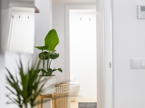 Eine Pflanze in einem weißen Topf auf einem Holzschemel, ein Korbwäsche und eine weiße Tür in einem Flur.