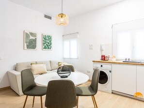 A modern kitchen with a washing machine, a dining area with a round table and chairs, and a living area with a sofa. - Brisa de Verano by Cadiz Time (Cádiz)