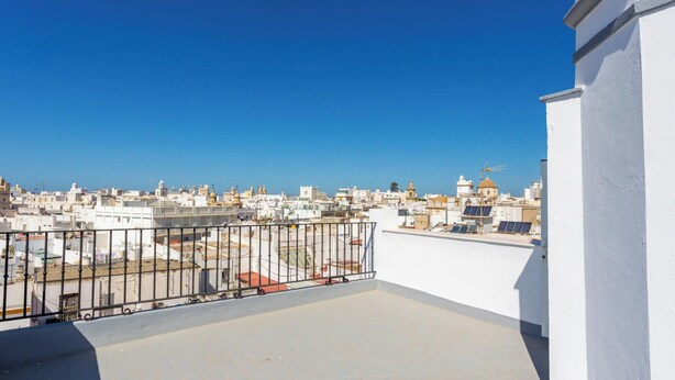 Vue panoramique d’une ville depuis le toit d’un immeuble, avec des bâtiments, un ciel bleu dégagé et un bâtiment blanc sur la droite.