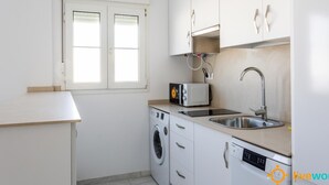 Une cuisine compacte équipée d’un lave-linge, d’un four à micro-ondes, d’un évier et d’une fenêtre.