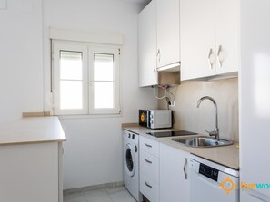 Une cuisine compacte équipée d’un lave-linge, d’un four à micro-ondes, d’un évier et d’une fenêtre.