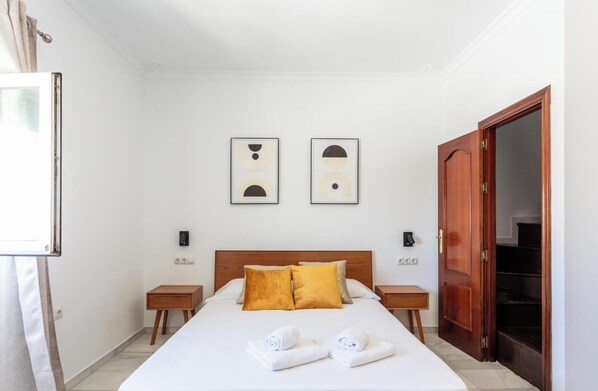 Une chambre d’hôtel comprenant un lit, deux tables de chevet, une armoire en bois et deux œuvres d’art abstraites accrochées au mur.