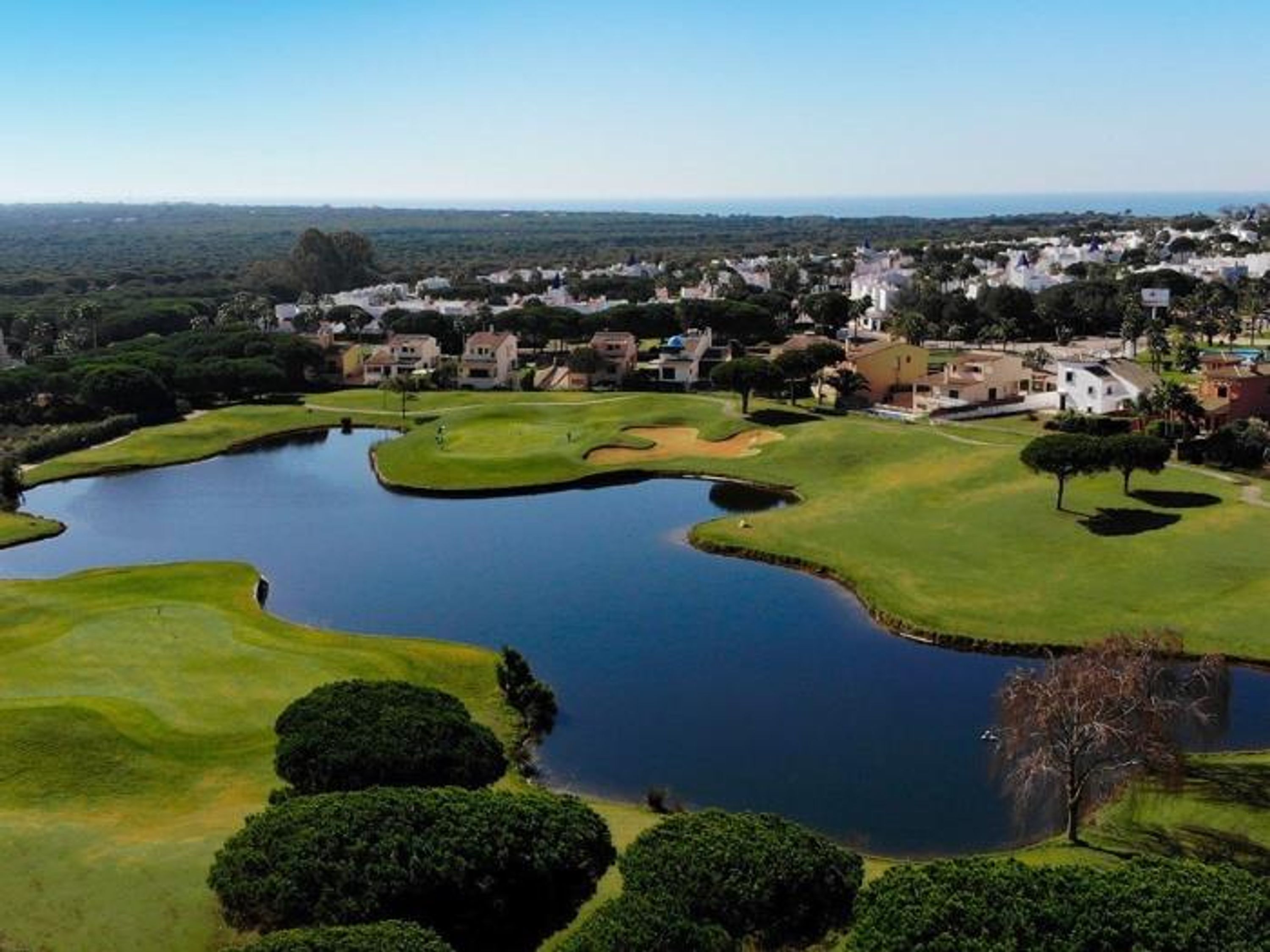 A golf course with a pond, surrounded by residential buildings.