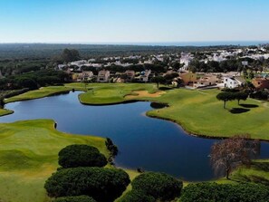 A golf course with a pond, surrounded by residential buildings. - Retama Golf by C diz Time (Chiclana de la Frontera)