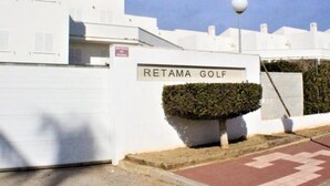 Schild für Retama Golf, ein weißes Gebäude mit befestigter Auffahrt und einer Hecke.