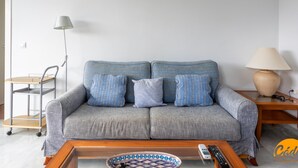 Ein Wohnzimmer mit grauem Sofa, blau-weißen Kissen, einem Holztisch, einer Stehlampe und einem Beistelltisch mit Lampe.