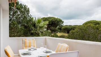 A dining area with a table set for four, surrounded by chairs with striped cushions, overlooking a lush landscape with trees and hills.