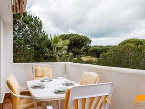 A dining area with a table set for four, surrounded by chairs with striped cushions, overlooking a lush landscape with trees and hills. - Retama Golf by C diz Time (Chiclana de la Frontera)