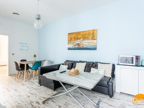 Ett modernt vardagsrum med en soffa, ett matbord och stolar. Det finns en tavla på väggen och en mikrovågsugn på bänkskivan.
