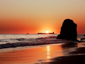 A sunset over a beach with a large rock formation. - Apartamento Atardecer by Cadiz Time (Chiclana de la Frontera)