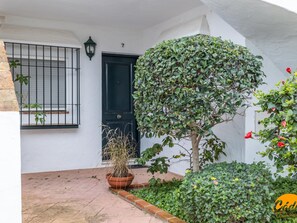 A white building with a black door, a potted plant, and a small garden area. - Apartamento Atardecer by Cadiz Time (Chiclana de la Frontera)