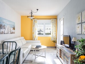 A living room with a white sofa, a round coffee table, a TV on a wooden stand, and a painting on the wall. - Apartamento Atardecer by Cadiz Time (Chiclana de la Frontera)
