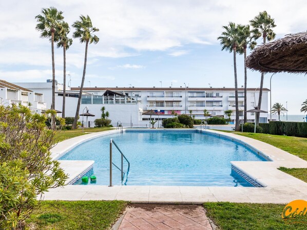 A swimming pool surrounded by palm trees and a building with balconies. - Apartamento Atardecer by Cadiz Time (Chiclana de la Frontera)