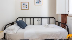A single bed with a black metal frame, white bedding, and a blue pillow. There are two framed artworks on the wall above the bed. - Apartamento el Patio by C diz Time (Cádiz)