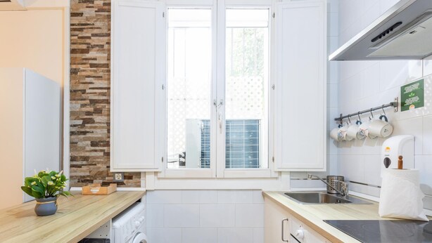 A compact kitchen with a built-in oven, a washing machine, a sink, and a window with blinds. - Apartamento el Patio by C diz Time (Cádiz)
