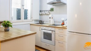 A modern kitchen with white cabinets, a stainless steel range hood, a built-in oven, a refrigerator, and a window with a view of greenery. - Apartamento el Patio by C diz Time (Cádiz)
