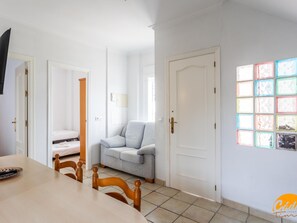 A room with a dining table, chairs, a sofa, a bed, and a door. - Apartamento Sol by C diz Time (Conil de la Frontera)